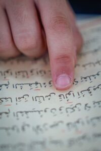 Student practicing Hebrew with a tutor through a laptop while reading notes and Hebrew text.
