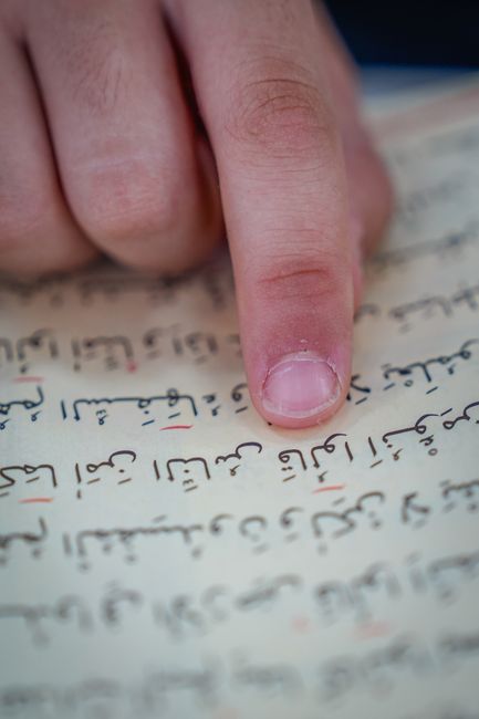 Student practicing Hebrew with a tutor through a laptop while reading notes and Hebrew text.