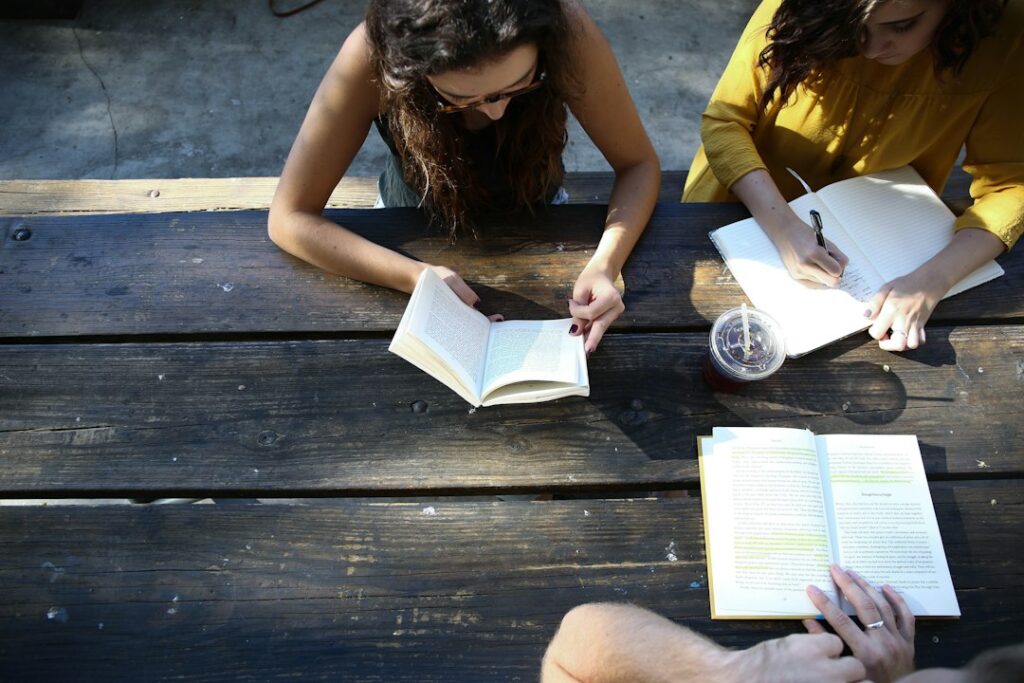 Adults sit around a table with Hebrew books, notebooks, and dictionaries during a friendly reading discussion.