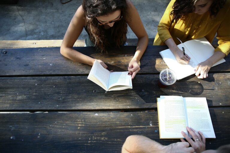 Adults sit around a table with Hebrew books, notebooks, and dictionaries during a friendly reading discussion.