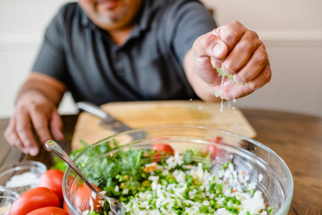 Adults and children prepare Israeli salad together while reading Hebrew recipe words in a home kitchen.