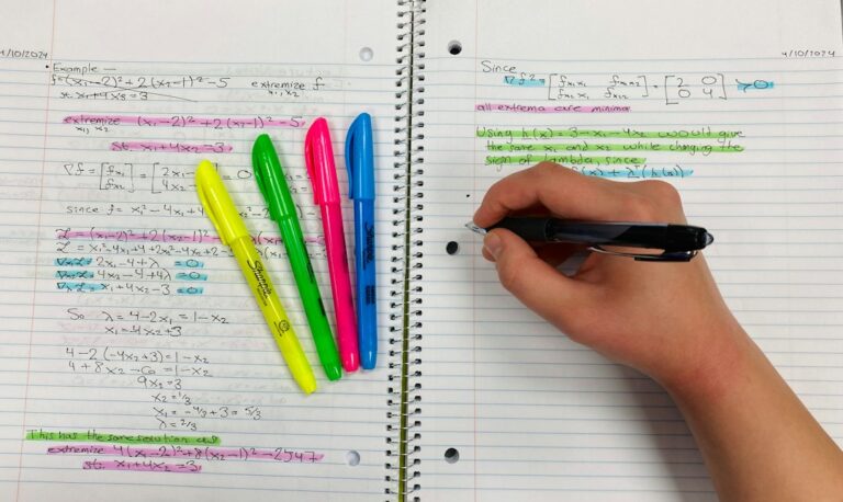 Learner writing Hebrew verb forms in a notebook beside a grammar chart and open Hebrew text.