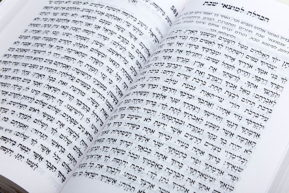 A learner reads Hebrew letters aloud beside a notebook, pencil, and open language workbook at a home desk.