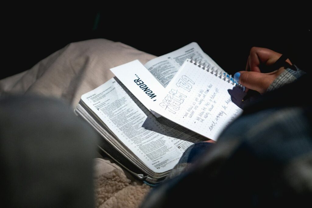 Person practicing Hebrew letters in a notebook beside an open language book and handwritten vocabulary cards.