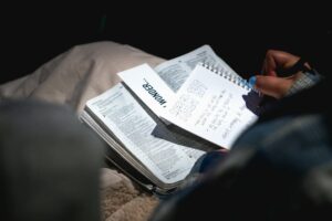 Person practicing Hebrew letters in a notebook beside an open language book and handwritten vocabulary cards.
