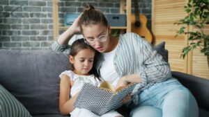 Adult and child reading a Hebrew book together at a kitchen table with notebooks and handwritten vocabulary nearby