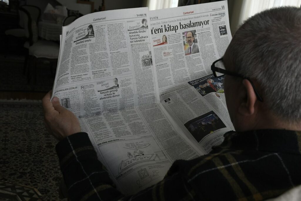 A Hebrew learner reads a news article beside a notebook while listening to an audio report.