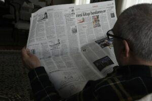 A Hebrew learner reads a news article beside a notebook while listening to an audio report.