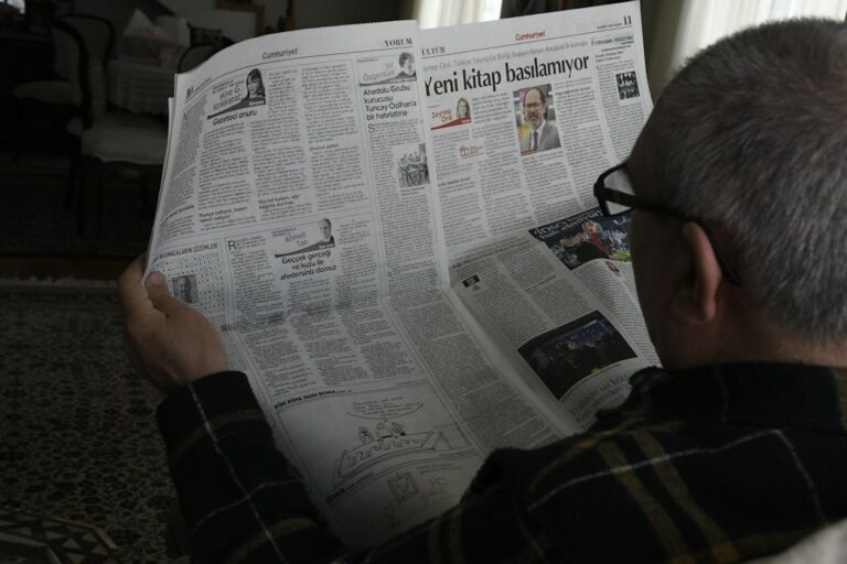 A Hebrew learner reads a news article beside a notebook while listening to an audio report.