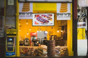 A learner practices Hebrew food-ordering phrases beside a menu, notebook, and cup of tea.