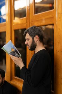 Person reading a Hebrew menu at a table beside a plate of food and a glass of water