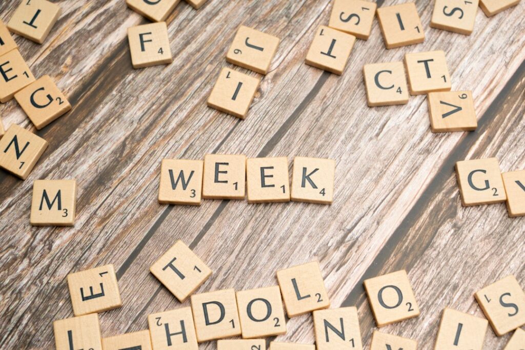 A student points to Hebrew weekday names on a calendar beside a notebook and pencil.