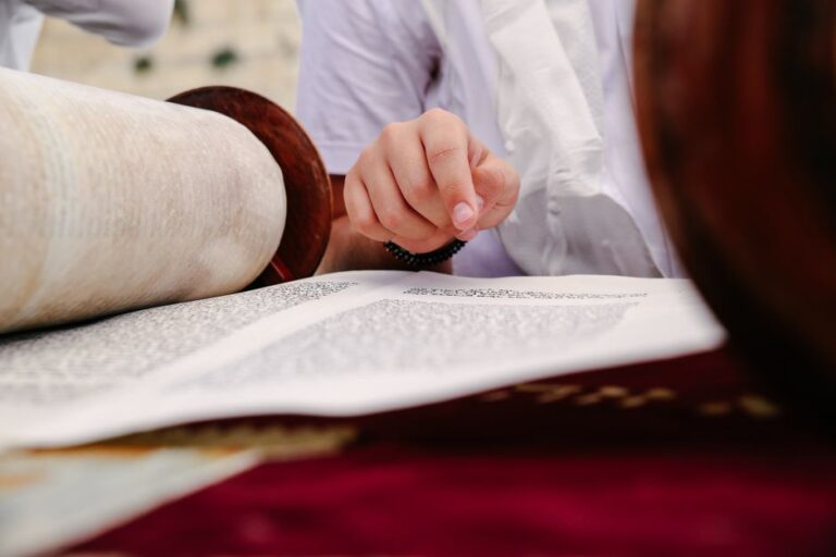 A learner compares a Hebrew Bible page with a modern Hebrew workbook at a study table.