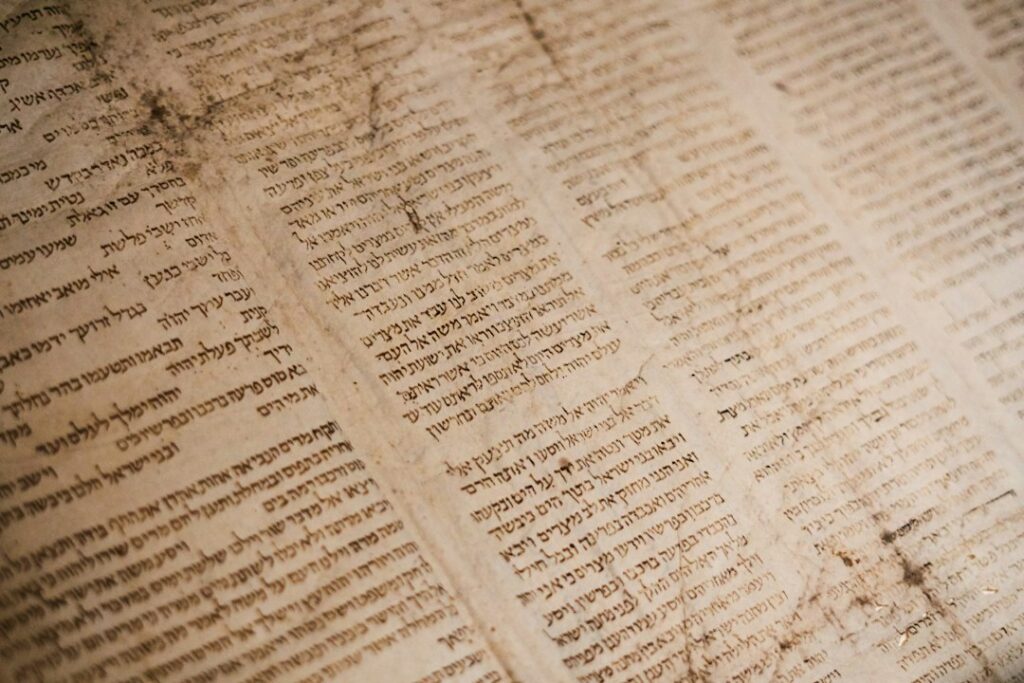 A learner reads a Hebrew newspaper at a table beside a notebook, dictionary, and pen.