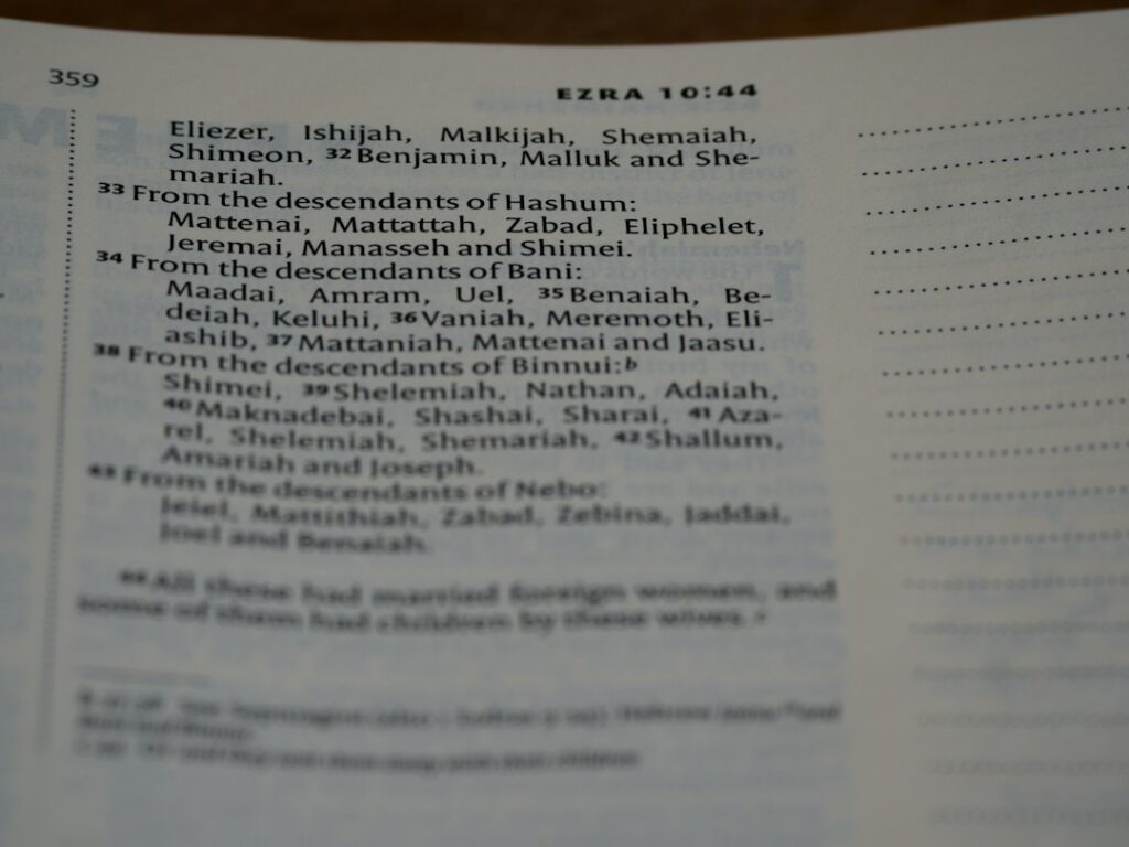 A person writes a name in Hebrew beside its English spelling in an open notebook.