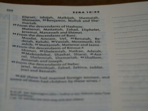 A person writes a name in Hebrew beside its English spelling in an open notebook.