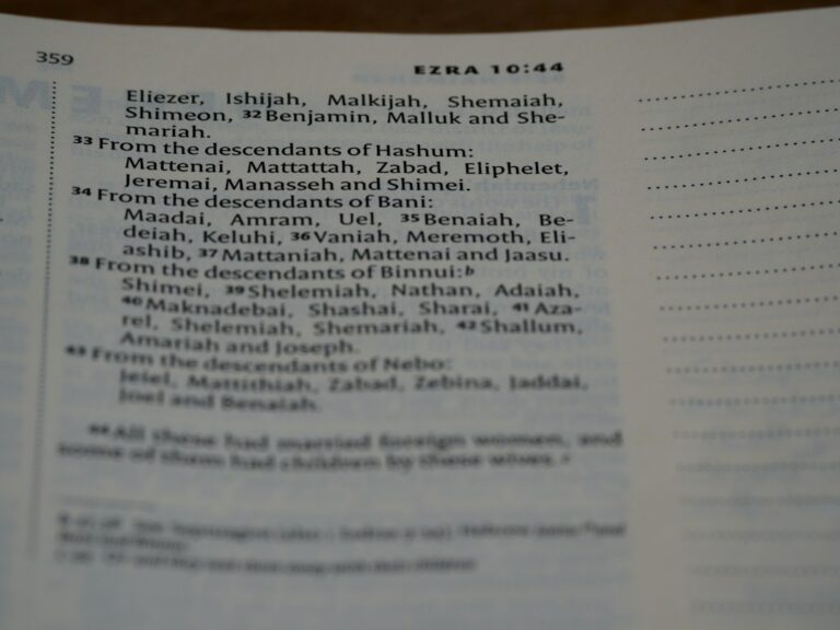A person writes a name in Hebrew beside its English spelling in an open notebook.