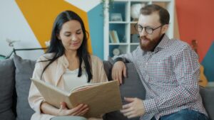 A beginner practices Hebrew phrases from handwritten notes with a conversation partner at a kitchen table.