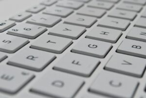 A learner types Hebrew on a laptop beside a phone displaying a right-to-left message.