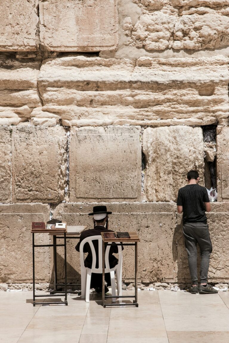 Traveler studies a Hebrew phrase card while speaking with a local person at a busy outdoor market.
