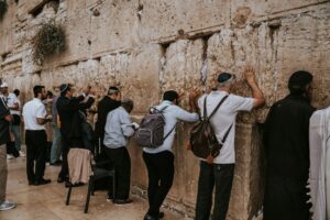 Two people greet each other beside a table with Hebrew notes, tea, and a small phrase guide.