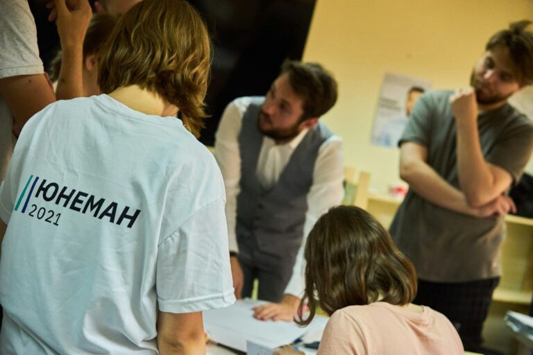 Two adults practice Hebrew emotion phrases together at a table with notebooks and handwritten vocabulary cards.