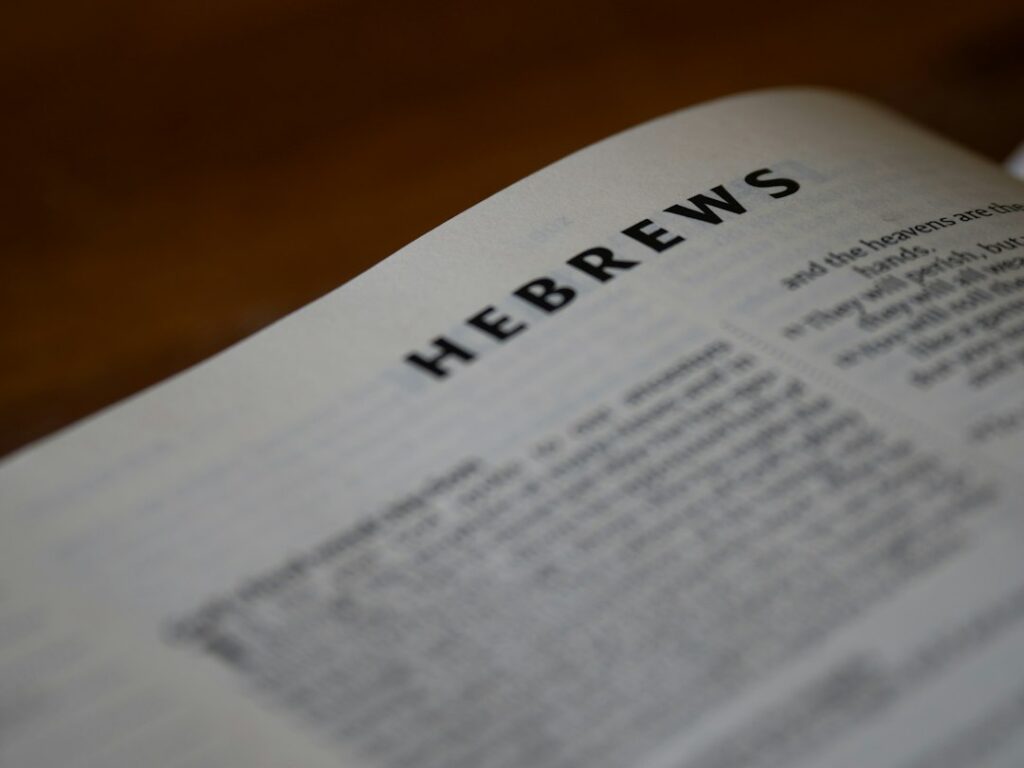 Children and adults read Hebrew together around a table with books, notebooks, and holiday objects.
