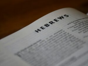Children and adults read Hebrew together around a table with books, notebooks, and holiday objects.