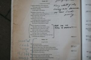 Two adults practice Hebrew greetings from a notebook at a kitchen table.