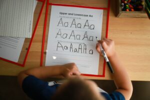 Student practicing right-to-left Hebrew letters on lined paper with a pencil and alphabet reference sheet.