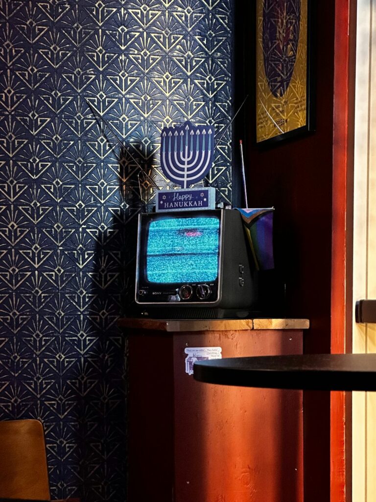 Adults watch a Hebrew comedy program with notebooks and subtitles visible on a living-room screen.