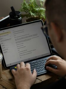 A learner types Hebrew on a tablet beside handwritten Hebrew letters and a language notebook.