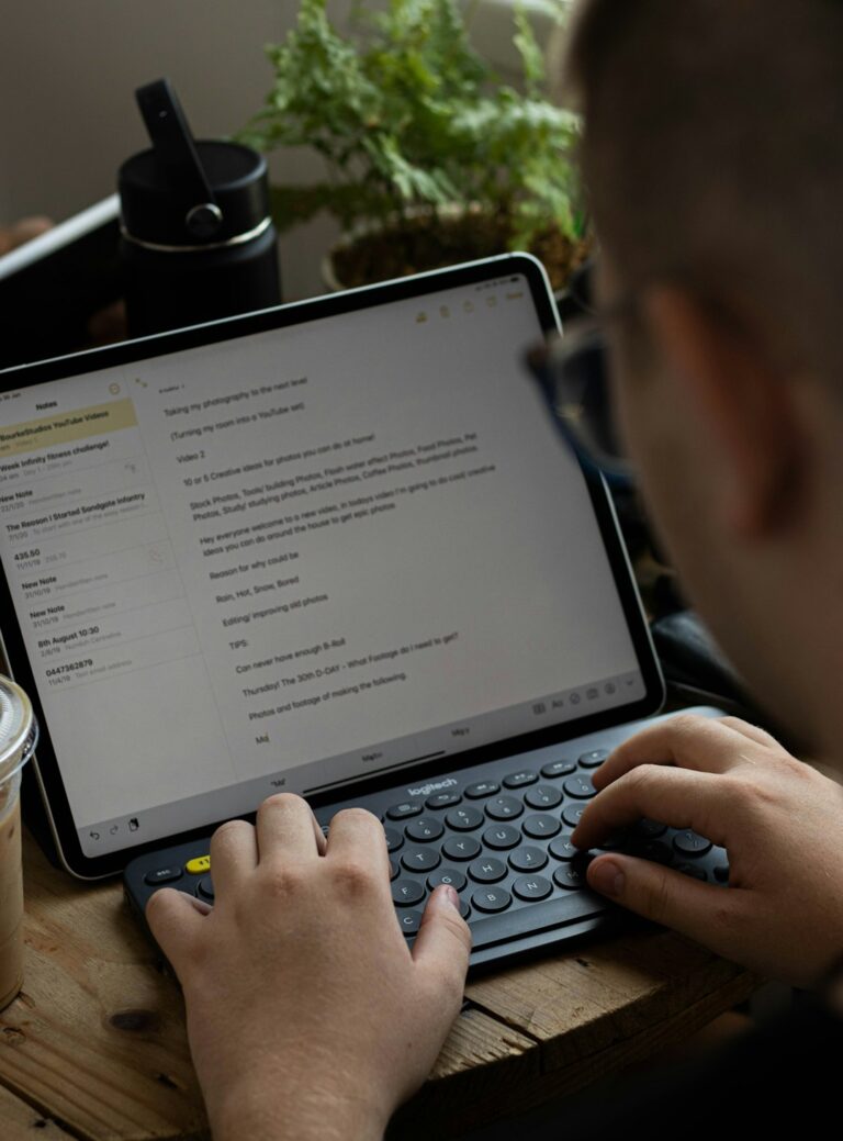 A learner types Hebrew on a tablet beside handwritten Hebrew letters and a language notebook.