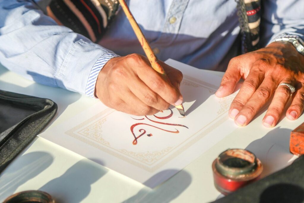A student writes Hebrew letters in a notebook beside a printed alphabet chart.