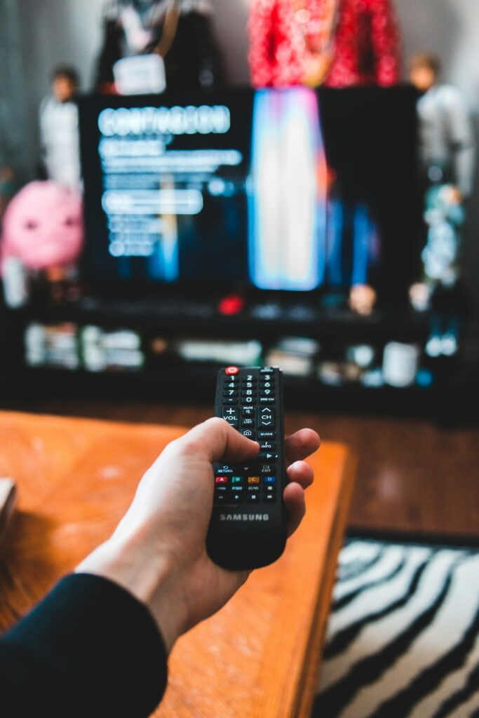 Adult learner watches a Hebrew television program with Hebrew subtitles and a notebook nearby.