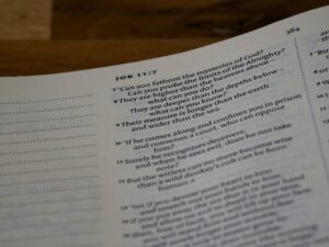 A student studies Hebrew prepositions from a workbook beside handwritten examples and a Hebrew alphabet chart.