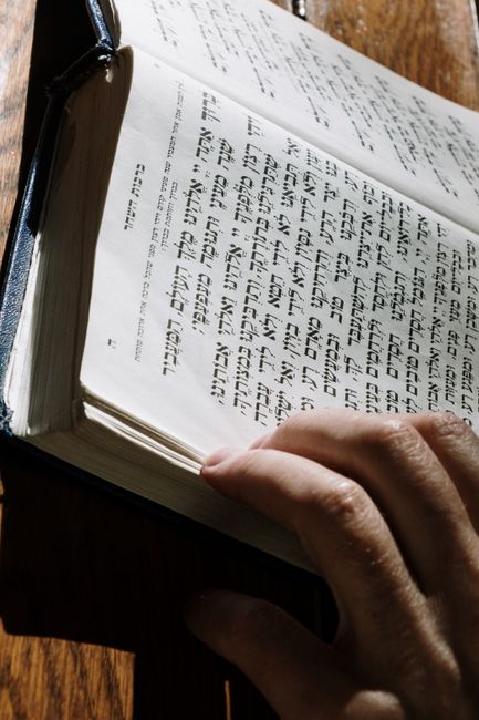 Students compare Hebrew prayer texts while practicing different pronunciation traditions around a classroom table.