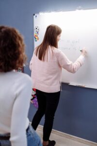 Two learners compare a casual Hebrew dialogue with a formal written message at a table.