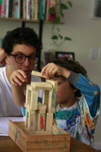 Parent and child practice Hebrew letters together at a kitchen table with cards, books, and colorful pencils.
