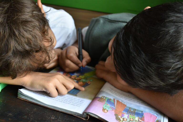 Parent and child read a Hebrew picture book together at a kitchen table with colorful illustrations visible.