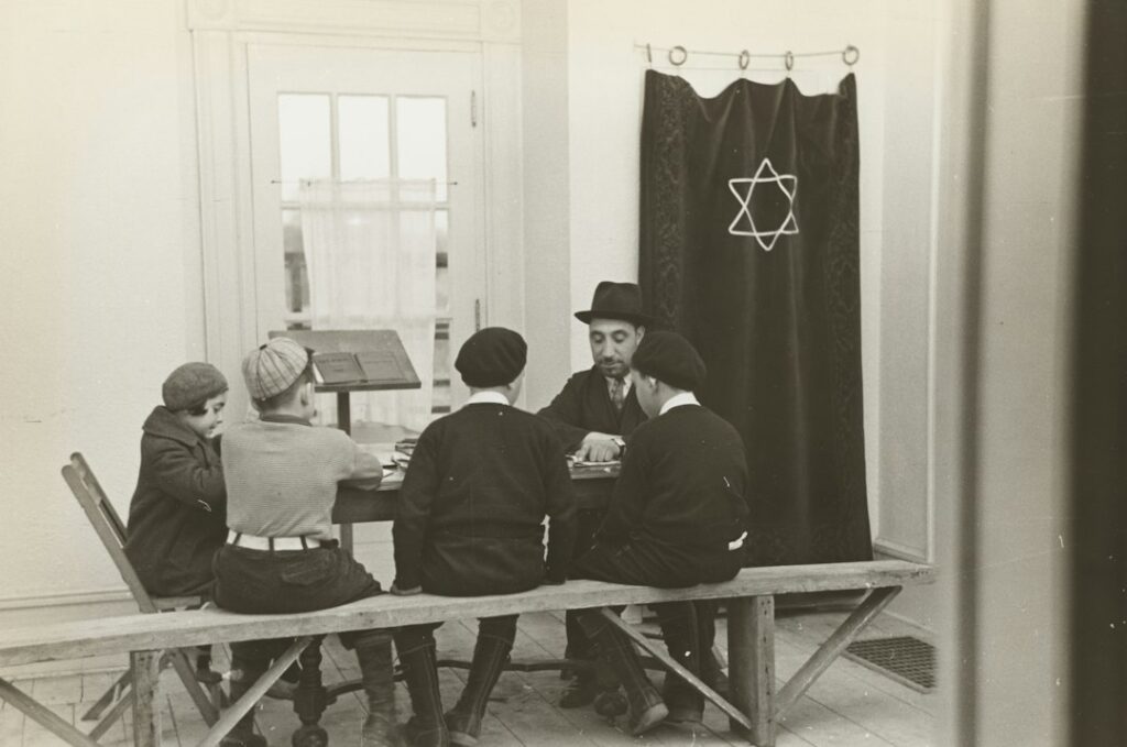 Students read Hebrew books together at a table with notebooks, vocabulary cards, and open language texts.