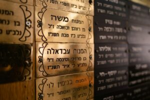 Adult learners practice Hebrew letters and conversation around a table with notebooks and printed text.
