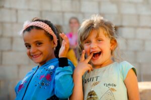 Children and an adult sing from Hebrew lyric sheets around a table with colorful alphabet cards.