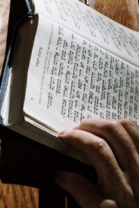 A learner reads an open Hebrew book beside handwritten vocabulary notes and a pencil.