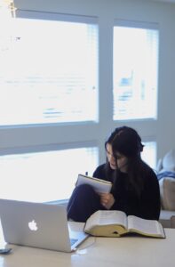 A learner reads Hebrew text at a table beside a notebook and handwritten vocabulary cards.