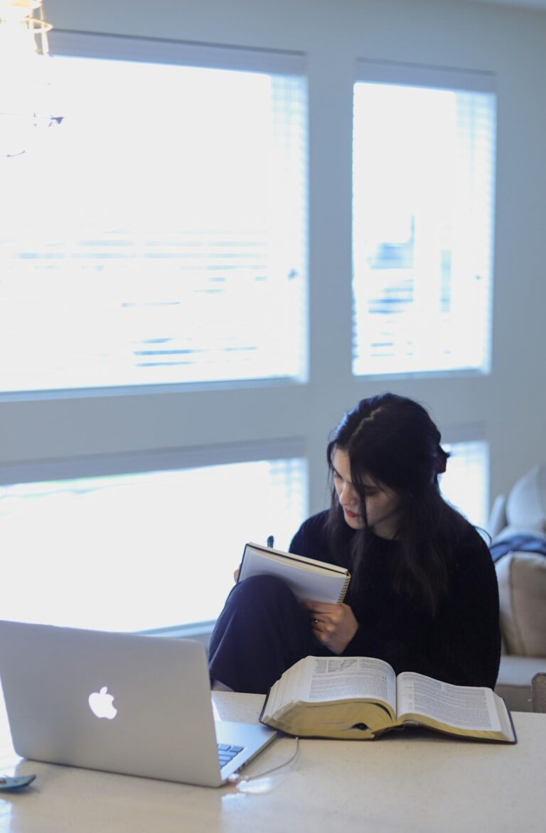 A learner reads Hebrew text at a table beside a notebook and handwritten vocabulary cards.