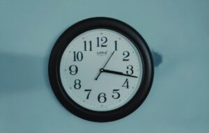 A learner studies Hebrew time expressions beside a clock, notebook, and handwritten Hebrew numbers.