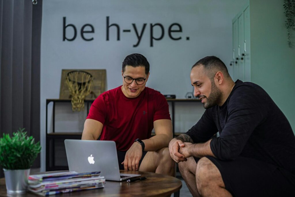Two professionals review Hebrew notes and a laptop during a workplace conversation.