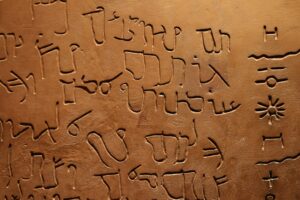 Person writing a personal name in Hebrew letters beside an open Hebrew alphabet guide.